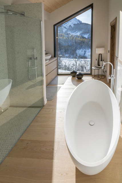 Grande salle de bains lumineuse avec bac à douche, baignoire, ameublement bois, fenêtre donnant sur un paysage enneigé