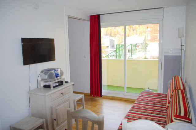 Séjour lumineux avec canapé, TV, porte-fenêtre, balcon et rideaux