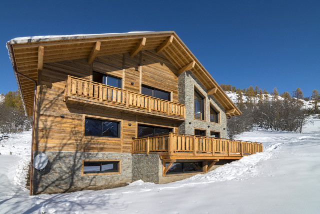 Grand chalet en bois et pierre sur deux étages, nombreuses fenêtres et large terrasse, balcon au 1er étage - © M Desvignes Grand chalet en bois et pierre sur deux étages, nombreuses fenêtres et large terrasse, balcon au 1er étage