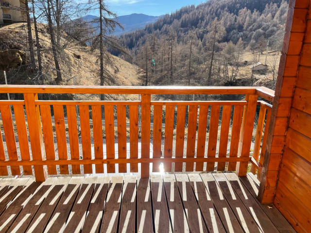 Wooden sunlit terrace with fence, unobstructed view of an autumn forest