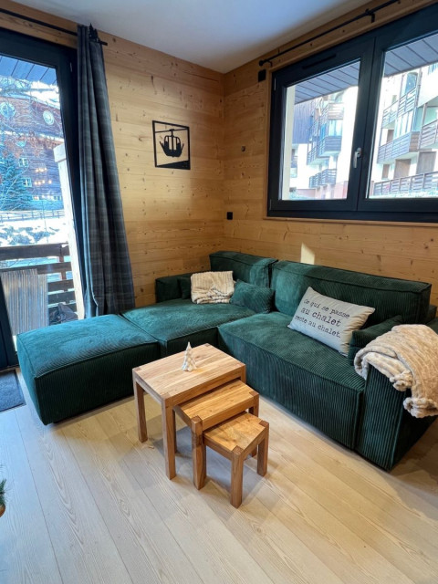 Séjour lumineux avec canapé, table basse, fenêtres donnant sur un balcon