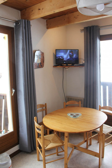 Bright living room with dining table, TV, windows and curtains, wooden balconies