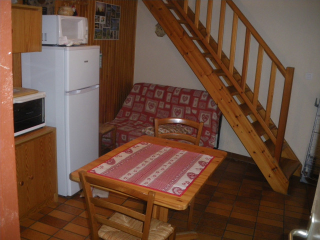 Coin séjour et cuisine avec table à manger, canapé, four à micro-ondes, TV, ameublement bois et parquet au sol, escalier vers l'étage supérieur - © J Matheron Coin séjour et cuisine avec table à manger, canapé, four à micro-ondes, TV, ameublement bois et parquet au sol, escalier vers l'étage supérieur