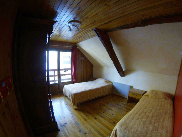 Chambre à coucher sous combles avec deux lits simples, fenêtre, ameublement bois, parquet