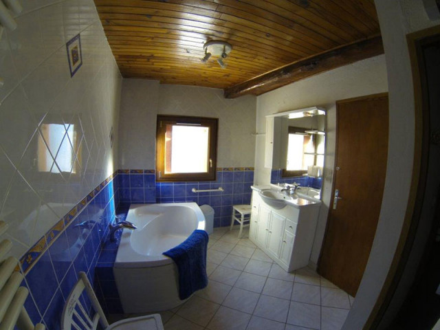 Salle de bains lumineuse, carrelée, avec baignoire, ameublement bois, fenêtre