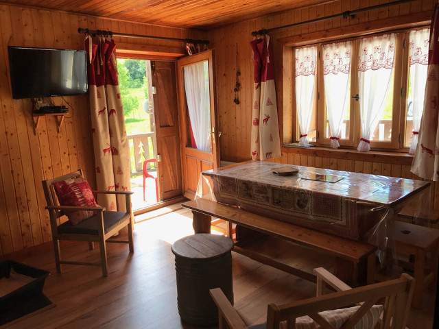 Salon de chalet avec table à manger, TV, fauteuil, porte vers terrasse, fenêtre