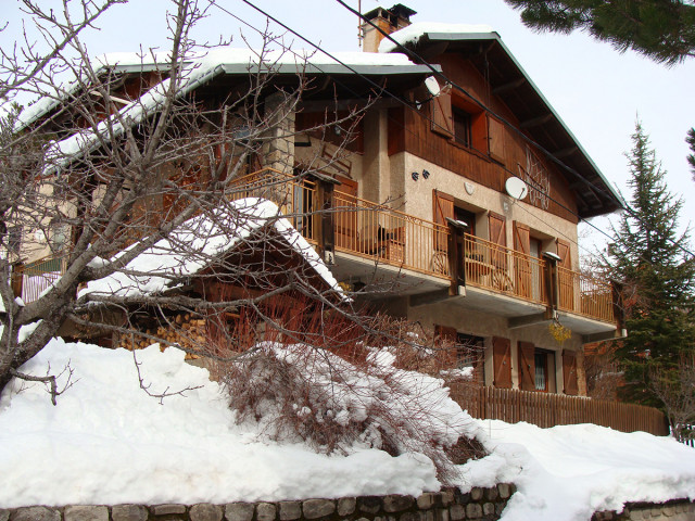 Vue de derrière d'une maison à 3 étages en bois et pierre, balcons métalliques et paysage enneigé