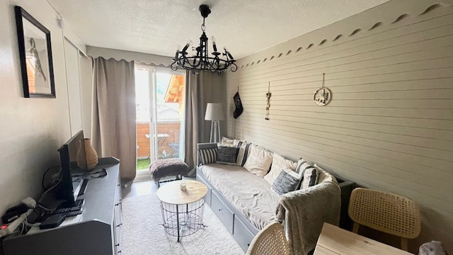 Bright apartment living room with sofa, armchair, coffee table, TV, and wooden furniture. French doors opening onto a balcony.