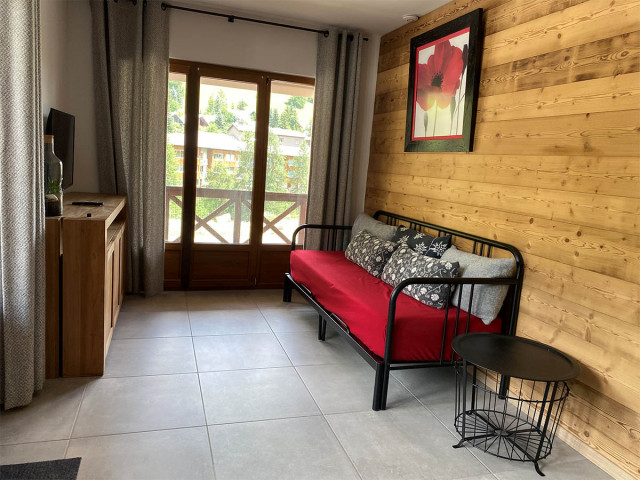 Salon d'appartement lumineux avec canapé, TV, ameublement bois, porte-fenêtre donnant sur un balcon