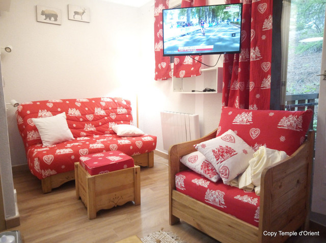 Séjour de studio lumineux confort avec canapé et fauteuils, TV, ameublement bois, fenêtre