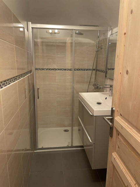 Salle de bains moderne carrelée avec bac à douche, évier et miroir, ameublement bois