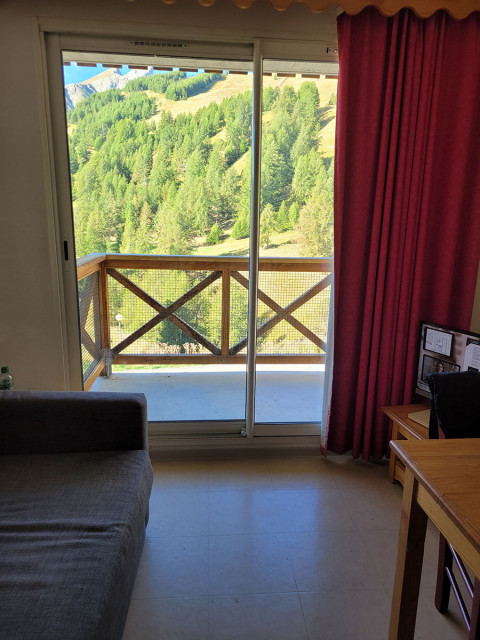 Séjour lumineux avec canapé, TV, ameublement bois, porte-fenêtre donnant sur un balcon avec vue sur les montagnes Séjour lumineux avec canapé, TV, ameublement bois, porte-fenêtre donnant sur un balcon avec vue sur les montagnes