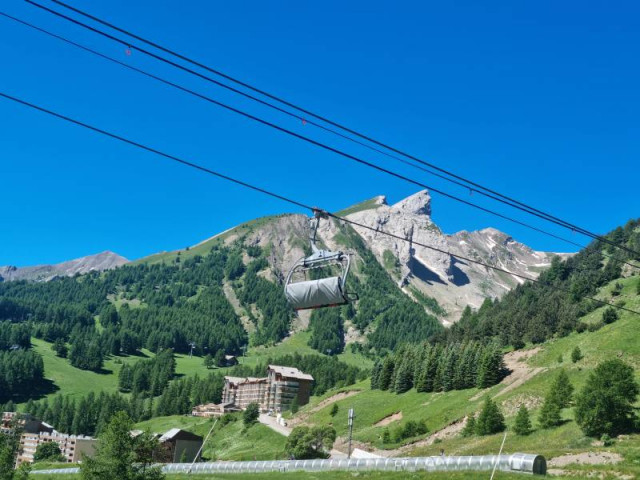 Télésiège au premier plan, paysage montagnard verdoyant avec quelques névés en altitude