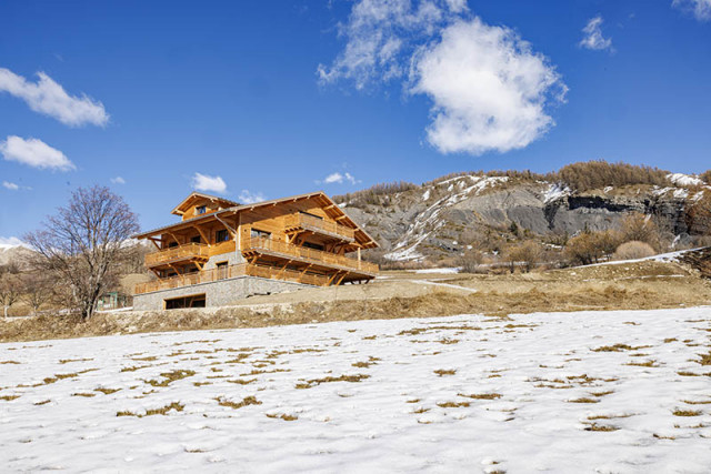 View of a three-storey chalet made of wood and stone, snow-capped mountain scenery