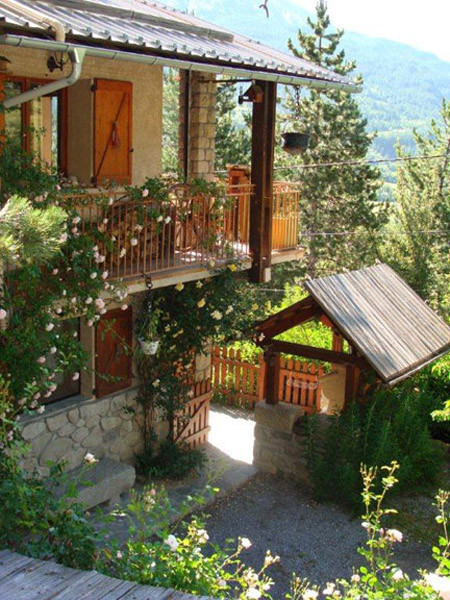 Side view of a three-storey house made of wood and stone with metal balconies, small inner courtyard, garden shed, spring landscape