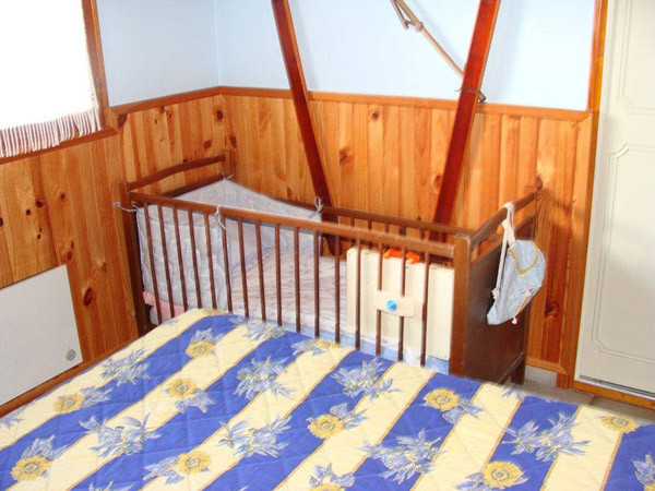 Bright children's bedroom with wooden furniture and wooden panelling, view of a single bed and cot