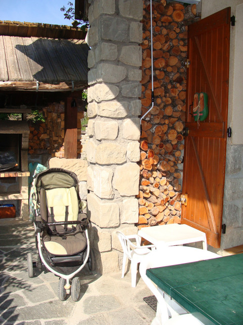 View of an outdoor terrace, wood pile, garden shed with an outdoor chimney used for barbecue, pushchair and outdoor table