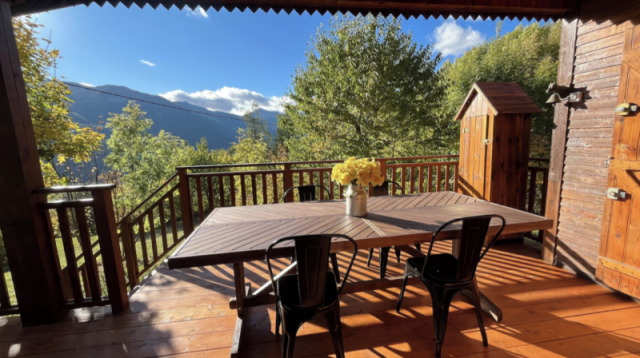 Terrazza in legno con tavolo in legno, sedie in ferro e un piccolo ripostiglio da giardino. Vista sulle montagne - © Estelle Rouhette Terrazza in legno con tavolo in legno, sedie in ferro e un piccolo ripostiglio da giardino. Vista sulle montagne
