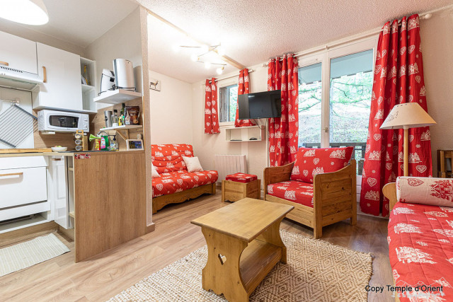 Séjour de studio lumineux avec canapé et fauteuils, table basse, coin cuisine équipé, ameublement bois, fenêtres