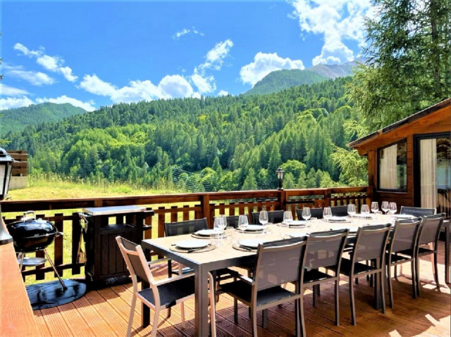 Wooden terrace at the chalet with large outdoor table, deckchair, veranda, unobstructed view with summer landscape