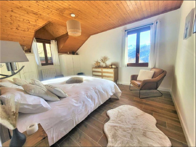 Chambre à coucher lumineuse avec lit double, ameublement bois, parquet au sol, fenêtres donnant sur les montagnes