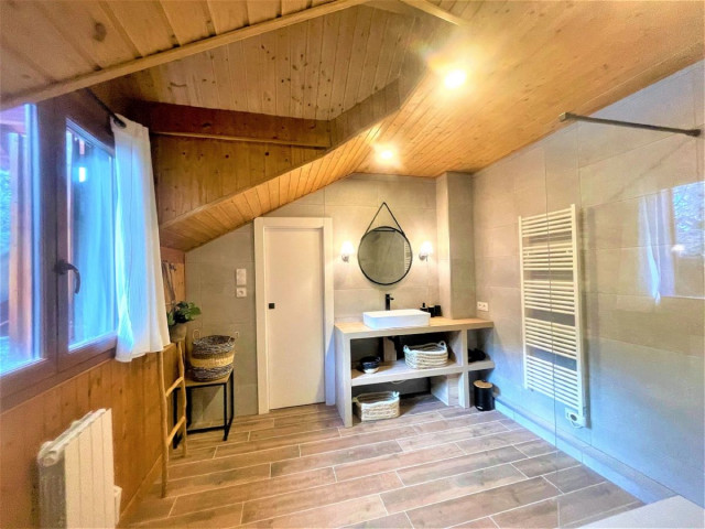 Salle de bains lumineuse avec grand bac à douche, ameublement bois, radiateur, parquet au sol, fenêtre