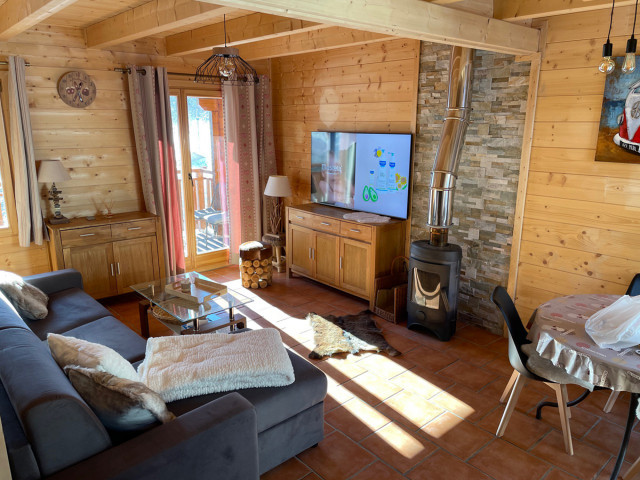 Séjour lumineux avec canapé, ameublement en bois, poêle à bois, TV, table à manger, fenêtres et rideaux