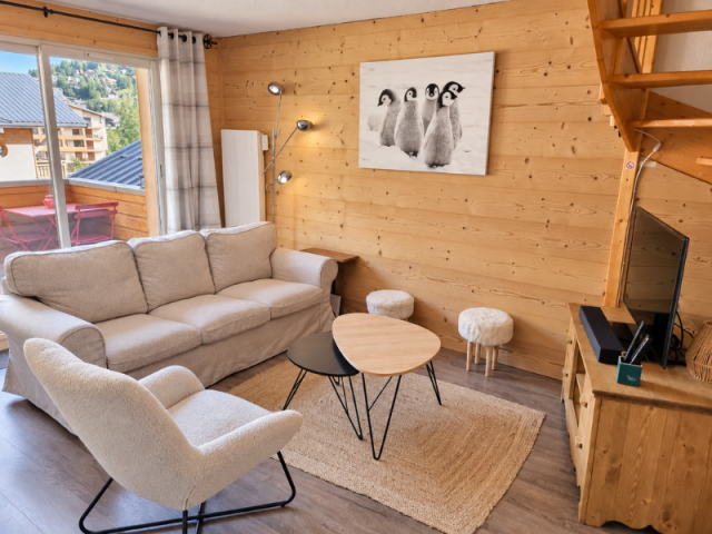 Salon chaleureux de style chalet, avec des murs en bois et des meubles aux tons beige et blanc. Une baie vitrée offre une vue sur les montagnes et les habitations voisines. - © C.Travaglini Salon chaleureux de style chalet, avec des murs en bois et des meubles aux tons beige et blanc. Une baie vitrée offre une vue sur les montagnes et les habitations voisines.